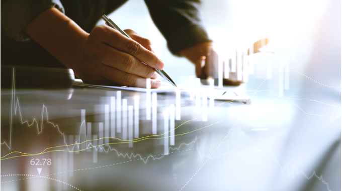 Pessoa escrevendo com caneta sobre tablet ou papel, com gráficos digitais de desempenho financeiro sobrepostos à imagem, representando análise de dados e crescimento de resultados.