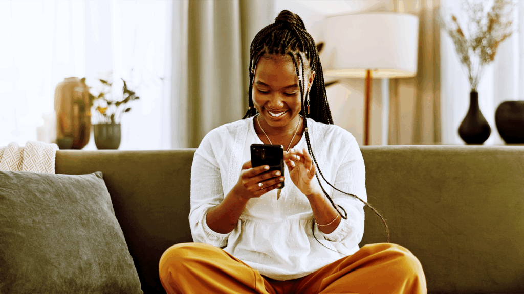 “Mulher sorridente sentada no sofá usando o celular para conversar com uma marca pelo WhatsApp, representando a experiência fluida e personalizada das campanhas Click to WhatsApp.