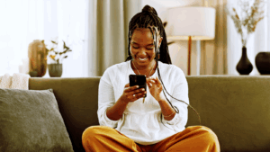 “Mulher sorridente sentada no sofá usando o celular para conversar com uma marca pelo WhatsApp, representando a experiência fluida e personalizada das campanhas Click to WhatsApp.